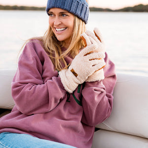 Woman wearing a blue knit hat with 'sota beanie' and pink sweater, sitting on a boat.