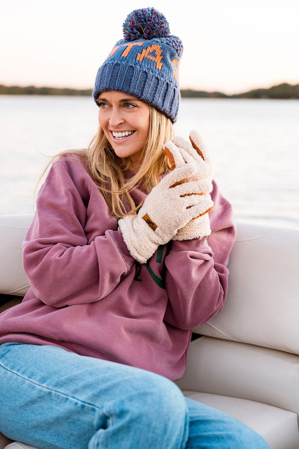 Woman wearing a blue knit hat with 'sota beanie' and pink sweater, sitting on a boat.