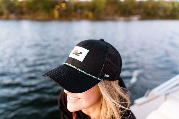 Woman wearing a black cap with a loon logo on a boat by a body of water