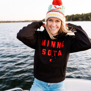 Person wearing a 'MINNESOTA' sweatshirt on a boat with a Minnesota Wild Hockey Team inspired beanie. There is a lake in the background.