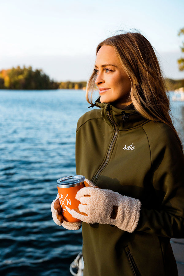Woman in a green jacket holding a coffee cup by a lake wearing Superior North hoodie by sota clothing