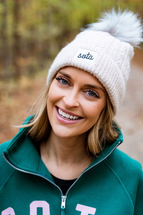 Woman wearing a sota beanie, walking in the woods.