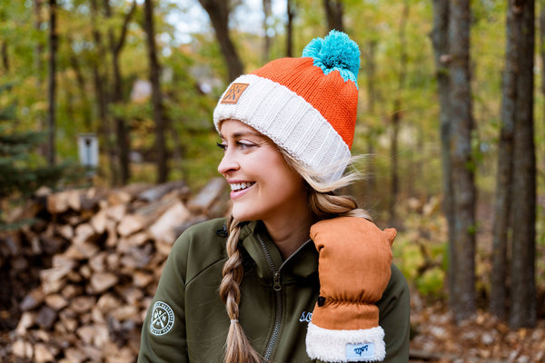Person wearing a colorful knit sota hat and green jacket in a forest setting