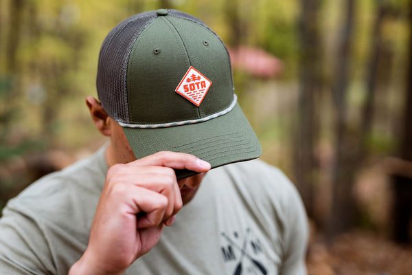 Man wearing a green cap with a Minnesota logo in a forest setting