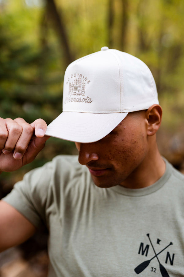 Person wearing a white cap with a logo and a green t-shirt with a design, standing in a forest.