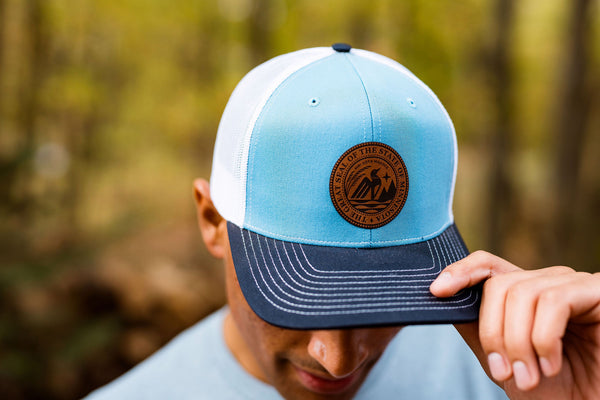 Person wearing a blue and white cap with a Minnesota State Seal logo against a blurred natural background