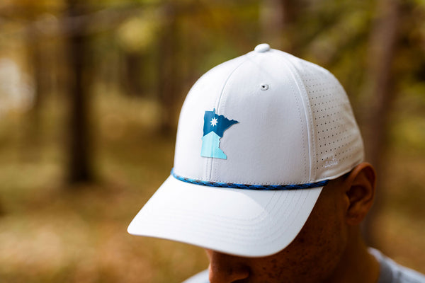 Grey Dri-fit baseball cap with a blue Minnesota logo worn by a person in a forest setting