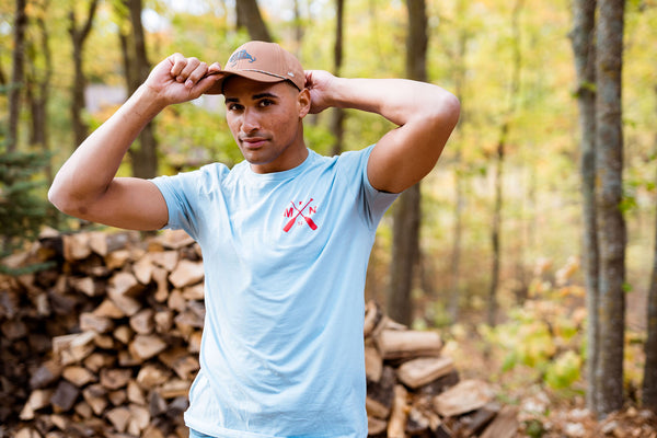 Man wearing a light blue t-shirt with a logo in a forest setting