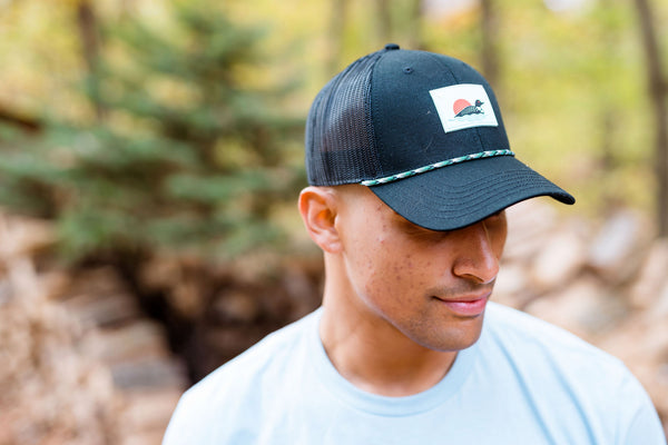 Person wearing a black cap with a loon logo in a forest setting