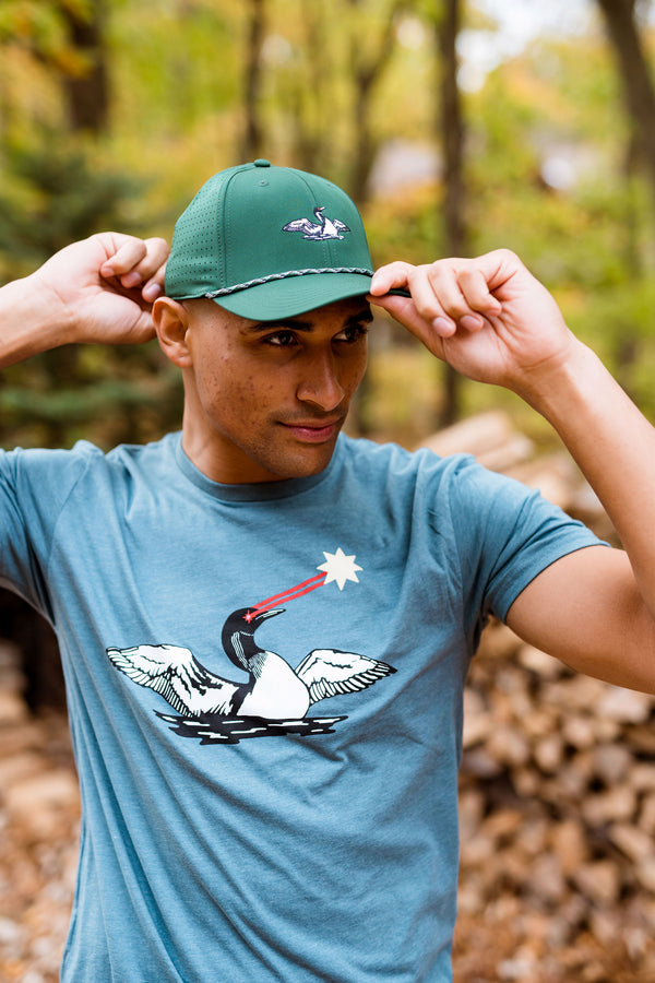 Man wearing a green cap with a laser loon logo in a forest setting