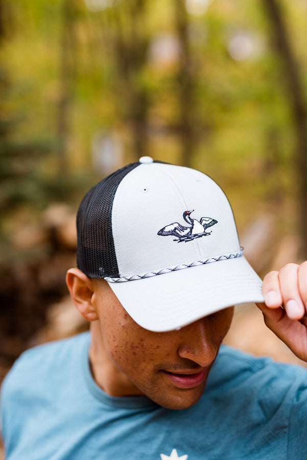 Man wearing a white and black cap with a laser loon logo, standing outdoors with a blurred natural background