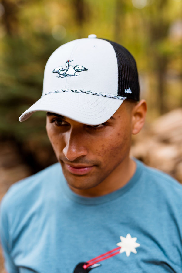 Man wearing a white and black cap with a laser loon logo, standing outdoors with a blurred natural background
