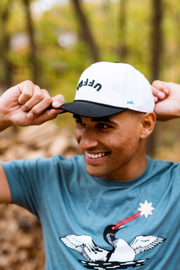 Man wearing a cap with an upside down UFFDA logo in a forest setting