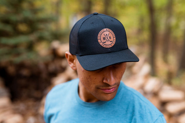 Man wearing a blue t-shirt with a laser loon graphic design and a minnesota-centric black cap with hockey sticks  in a forest setting