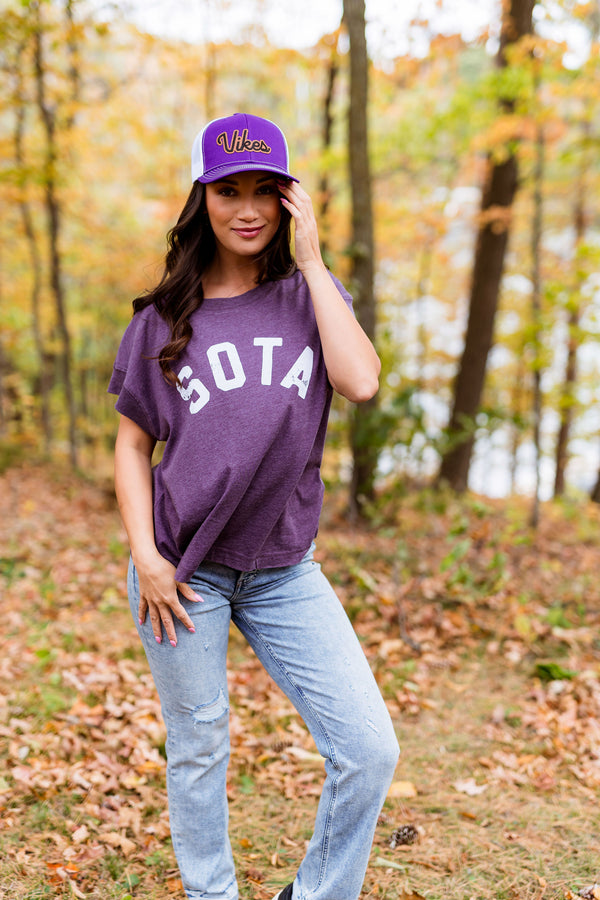 Woman wearing a purple 'SOTA' t-shirt and cap in an autumn forest.