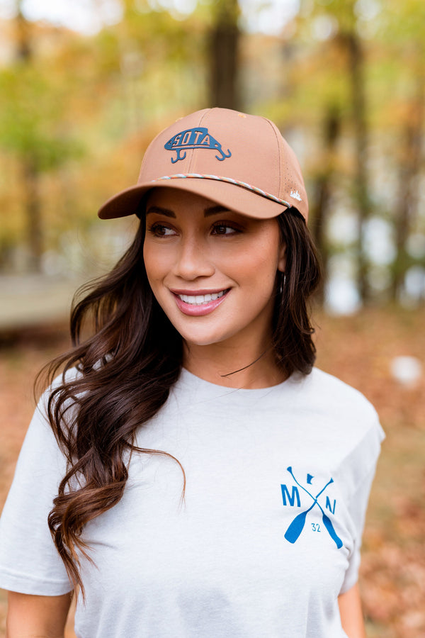 Woman wearing a tan cap and white t-shirt with a Minnesota logo in an outdoor setting