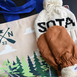 Tote bag with nature design, beanie with 'SOTA' text, and brown mittens on a dark surface