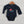 Navy blue baby onesie with a red sun and black loon design on a wooden hanger against a white brick wall.